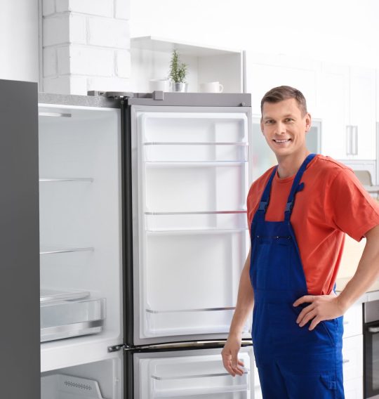 Male technician in uniform near refrigerator indoors